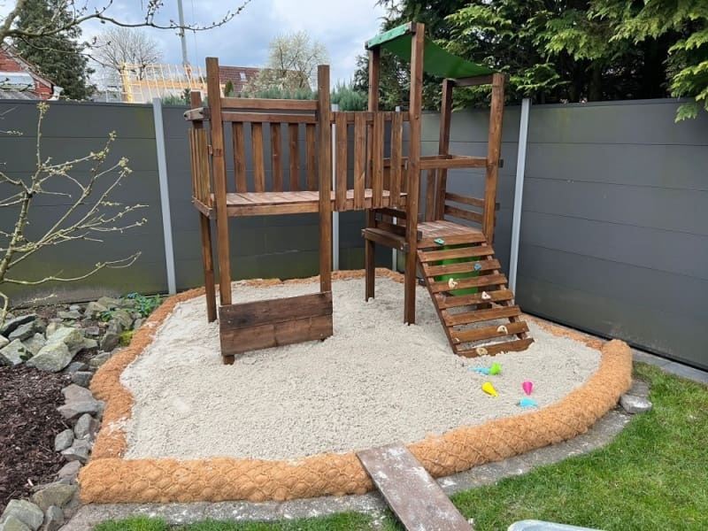 Kokosové válce Coir Log instalové na okrajích dětského pískoviště s prolézačkou. Foto ze zahrady