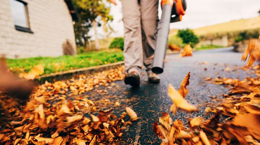Muž odklízející listí z cesty pomocí fukaru